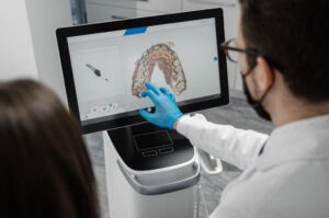 Ein männlicher Arzt zeigt die Ergebnisse eines digitalen intraoralen Scans der Zähne des Patienten in 3D. Zahnarzt zeigt mit dem Finger auf den Bildschirm