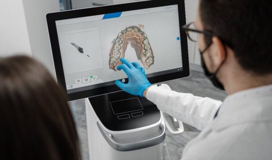 Ein männlicher Arzt zeigt die Ergebnisse eines digitalen intraoralen Scans der Zähne des Patienten in 3D. Zahnarzt zeigt mit dem Finger auf den Bildschirm