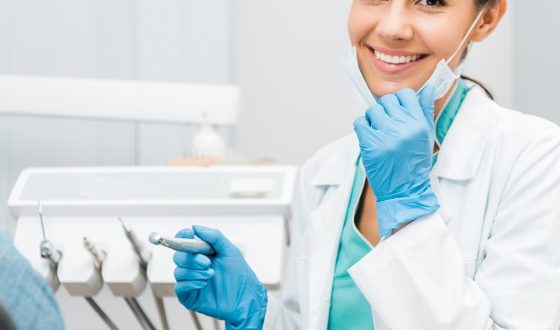 Fröhliche Zahnärztin hält Bohrer in der Hand und lächelt neben dem Patienten