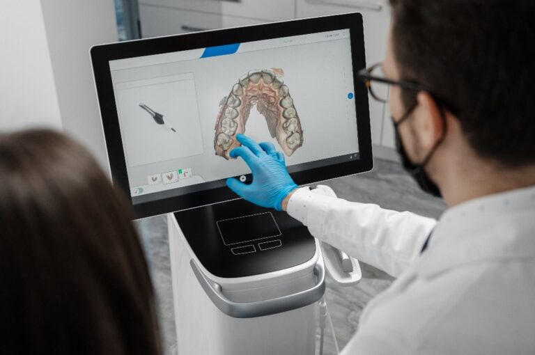 Ein männlicher Arzt zeigt die Ergebnisse eines digitalen intraoralen Scans der Zähne eines Patienten in 3D auf dem Display.